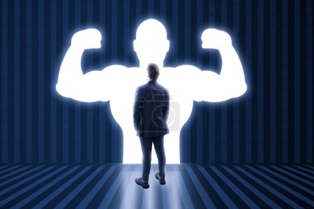 Back view of man with very strong illuminated shadow flexing muscles on dark wall background. Personal development, inner strength, motivation concept