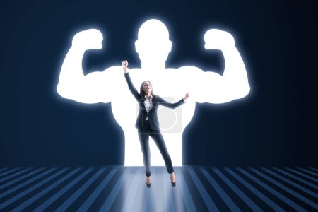 Happy european businesswoman with very strong illuminated shadow flexing muscles on dark wall background. Personal development, inner strength, motivation concept