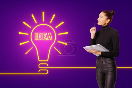 Eine Frau, die einen Notizblock in der Hand hält, scheint eine kreative Idee zu haben, die durch eine Neonröhre mit dem Wort IDEA auf lila Hintergrund angezeigt wird.