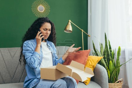 Photo for An upset and disappointed buyer in an online store, a woman is not satisfied with the received parcel of goods sits on the sofa and calls the online customer support service to complain. - Royalty Free Image