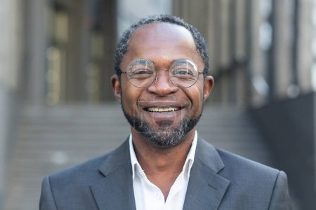 Photo for Close up photo portrait of successful and smiling African American man, businessman wearing glasses smiling and looking at camera from outside office building. - Royalty Free Image
