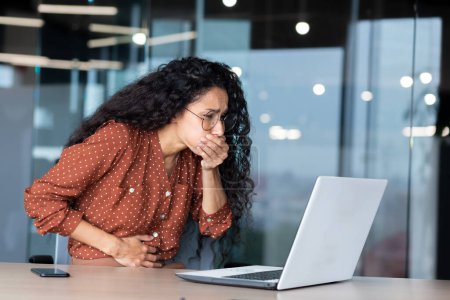Businesswoman has severe nausea, latin american woman at work sick, working sitting at table with laptop inside office.