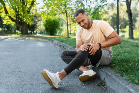 Téléchargez les photos : Man injured leg while jogging, african american man sitting on ground, massaging sore muscle with hands, upset and injured runner. - en image libre de droit
