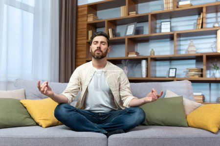 Téléchargez les photos : Mature man alone at home resting after work sitting in lotus position on sofa in living room meditating and relaxing. - en image libre de droit