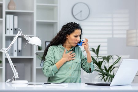 Téléchargez les photos : Attaque d'asthme chez les femmes d'affaires hispaniques à l'intérieur du bureau sur le lieu de travail avec ordinateur portable, la femme utilise un inhalateur avec des médicaments pour faciliter la respiration. - en image libre de droit