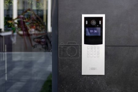 Entrance doorbell in a multi-apartment building, with a video surveillance camera, on a dark wall.