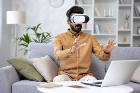 Photo for Surprised serious man in virtual reality glasses reviewing course in virtual meeting sitting on sofa in living room at home. - Royalty Free Image
