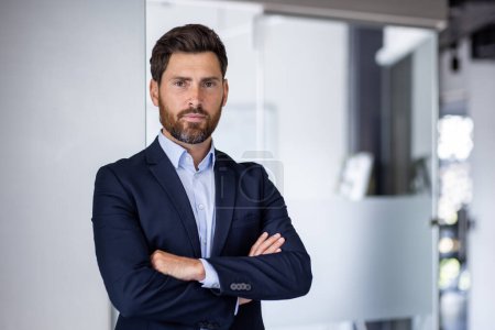 Portrait of mature experienced financier businessman, man thinking seriously looking at camera with crossed arms, confident investor banker inside office workplace in business suit.