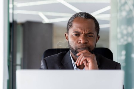 Photo for Close-up photo. Senior African American male businessman, director sits in the office at the laptop and looks thoughtfully at the screen. - Royalty Free Image
