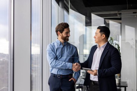 Foto de Dos hombres de negocios profesionales estrechando la mano en una oficina moderna, simbolizando la asociación, la colaboración y el acuerdo comercial exitoso. - Imagen libre de derechos