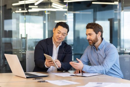 Foto de Dos hombres de negocios profesionales participaron en una discusión sobre tableta digital y portátil en un entorno de oficina corporativa. - Imagen libre de derechos