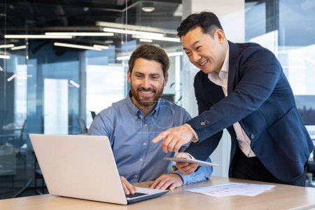 Foto de Dos hombres de negocios profesionales que trabajan juntos en un proyecto en la oficina, discutiendo sobre un ordenador portátil y tableta con entusiasmo. - Imagen libre de derechos