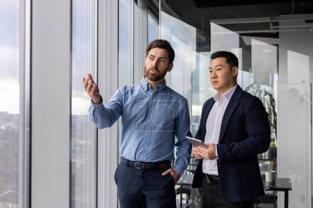Foto de Dos profesionales corporativos masculinos participan en una discusión seria sobre estrategias de negocio en su oficina bien iluminada. - Imagen libre de derechos