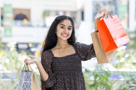 Femme indienne joyeuse portant des sacs à provisions tout en marchant dans un centre commercial. Profiter des plaisirs du shopping et de la sélection de cadeaux.