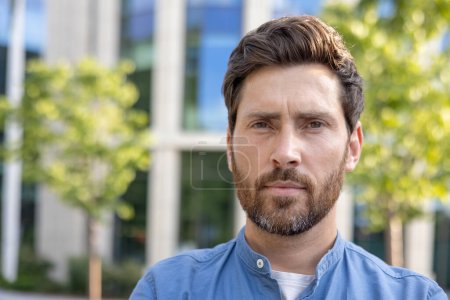 Homme d'affaires mature barbu en tenue décontractée debout à l'extérieur près d'un complexe de bureaux, respirant la confiance et le professionnalisme.