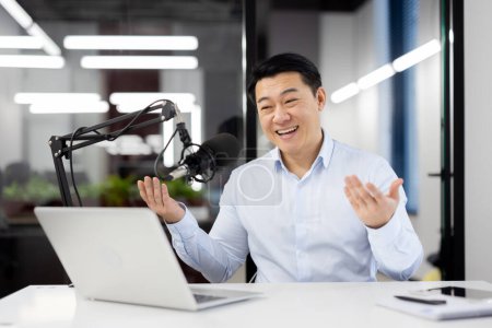 Ein begeisterter asiatischer Geschäftsmann nimmt einen Podcast in einem modernen Büroumfeld auf und bringt damit Glück und Professionalität zum Ausdruck.