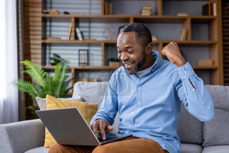 Fröhlicher afroamerikanischer Mann mit Laptop, der Erfolge feiert. Perfektes Image für Themen wie Leistung, Glück und Fernarbeit.