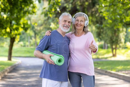 Cheerful senior man and woman in sportswear enjoying fitness lifestyle outdoors with yoga mat and headphones, showing thumbs up.