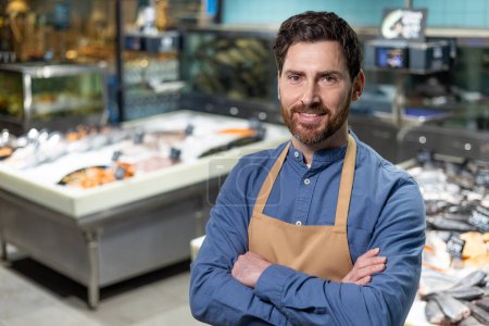 Portrait of a confident and experienced male shop worker, proudly standing in the seafood department of a supermarket. His friendly smile and professional apron suggest expertise and approachability