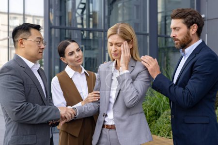 Photo for Concerned business colleagues provide comfort to a stressed female professional experiencing a headache outside a modern office building. - Royalty Free Image