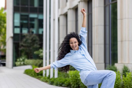Photo for An exuberant woman dances freely outside a modern building, embodying joy and liberation. She celebrates life with her dynamic movement, invoking feelings of happiness and spontaneity. - Royalty Free Image