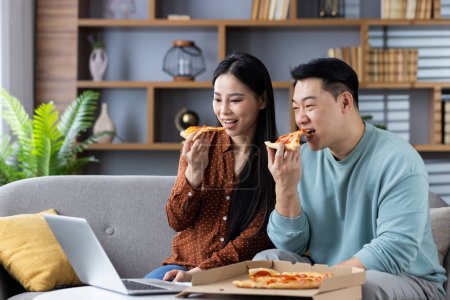 A casual and happy couple sharing pizza during a break from remote work in a cozy living room setting.