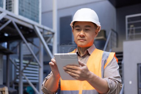 Konzentrierter asiatischer Ingenieur mit hartem Hut und digitalem Tablet am Industriestandort. Technologie und Engineering-Konzept.