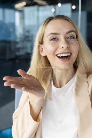 Foto de Alegre mujer de negocios rubia hablando y haciendo gestos, como en una discusión amistosa en un entorno de oficina moderno. - Imagen libre de derechos