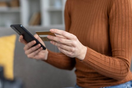 Ausgeschnittene Ansicht einer Person, die eine Kreditkarte und ein Smartphone in der Hand hält, was auf eine sichere Online-Zahlung oder mobile Banking-Transaktion hindeutet.