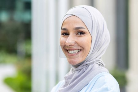 Un retrato de una mujer alegre con un hiyab, irradiando confianza y satisfacción con un fondo borroso.