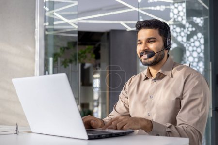 A professional man with a headset using a laptop in a modern office setting, conveying customer service and technology.