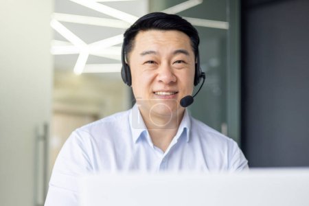 A professional Asian man is engaged in his work at a modern office, embodying dedication and focus.