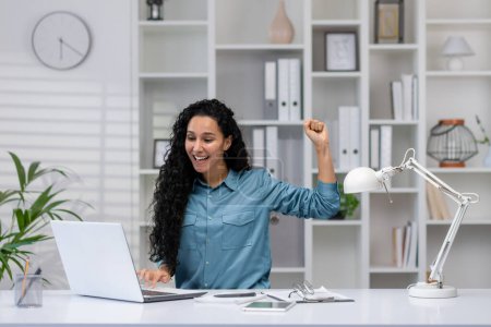 Téléchargez les photos : Femme hispanique excitée travaillant à partir d'un bureau à domicile célèbre une réalisation d'entreprise avec une pompe poing joyeux. - en image libre de droit