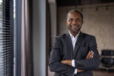 Porträt eines selbstbewussten afroamerikanischen Geschäftsmannes mit einem warmen Lächeln, der in einem modernen Büroumfeld steht.