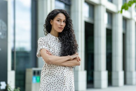 Portrait of a confident businesswoman with crossed arms standing outside of a contemporary office building, showcasing professionalism and strength.