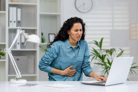 Professional woman experiencing discomfort while seated at a workstation, indicating possible health issues at work.