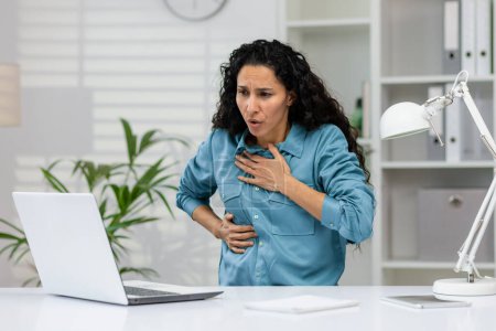 Gestresste Geschäftsfrau leidet unter starken Brustschmerzen, möglicherweise einem Herzinfarkt oder Angstzuständen, während sie an ihrem Schreibtisch im Büro arbeitet.