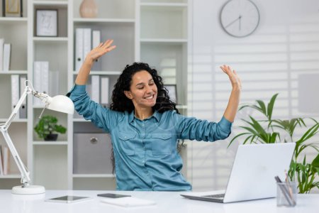 Photo for Joyful businesswoman with arms raised in excitement at her desk in a modern office, celebrating professional achievement. - Royalty Free Image
