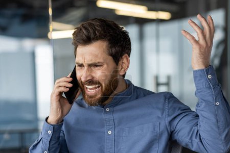 Ejecutivo masculino frustrado teniendo una conversación acalorada en un teléfono inteligente en un entorno de oficina moderno.