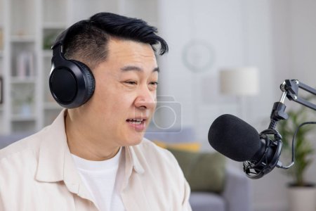 Asian male podcaster speaking into a microphone while recording content for his podcast in a cozy home studio setting.
