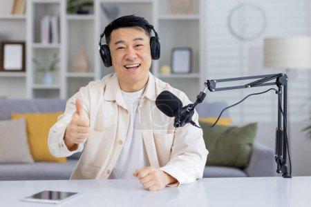 Photo for Cheerful Asian man in a headset with microphone giving a thumbs up while looking at the camera, indicating a positive conversation or successful podcast recording. - Royalty Free Image