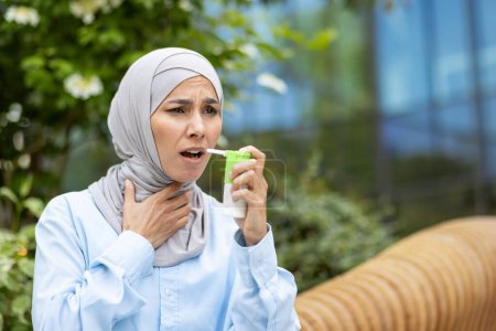 Diverse female with medical aerosol having pulmonary disease and using treatment for relieving bronchial spasms. Stressed lady wearing hijab and struggling with breath disability during stroll.