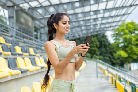 Foto de India joven mujer de los deportes de pie en el estadio tribuna fuera y el uso de teléfono sonriendo. Foto de primer plano. - Imagen libre de derechos