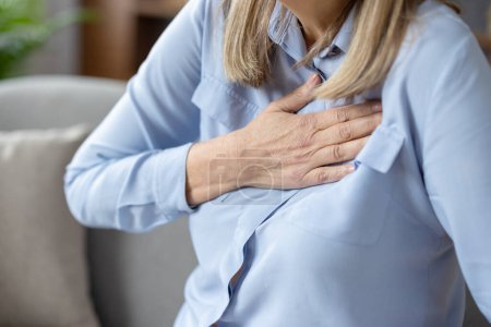 Image en gros plan d'une femme âgée souffrant d'inconfort et tenant sa poitrine, indiquant peut-être des problèmes cardiaques ou une crise cardiaque.