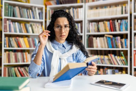 Eine seriöse Bibliothekarin mittleren Alters mit Brille untersucht sorgfältig ein Buch, während sie die Bücherregale organisiert, umgeben von einer umfangreichen Büchersammlung..