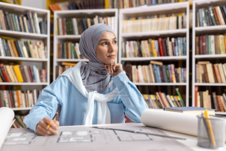 A thoughtful Muslim woman architect works with blueprints in a library setting, surrounded by books, showcasing dedication and expertise in her field.