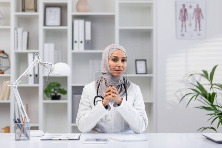 A professional portrait of a confident female doctor wearing a hijab, sitting in her well-organized clinic office, illustrating inclusivity and diversity in healthcare.