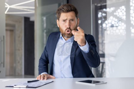 Ein professioneller Geschäftsmann mittleren Alters im blauen Anzug sieht frustriert aus und zeigt direkt in die Kamera, wahrscheinlich während einer hitzigen Videodiskussion.