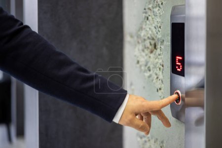 Foto de Un hombre de negocios profesional en un traje oscuro presionando un botón de ascensor, simbolizando la conveniencia y la vida corporativa moderna en un entorno urbano. - Imagen libre de derechos