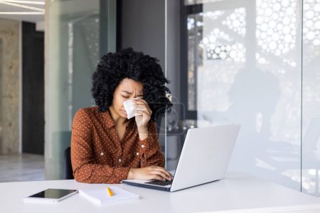 Photo for A young African American woman feeling emotional, crying at her office desk while working on a laptop, showcasing workplace stress and the challenges of professional life. - Royalty Free Image